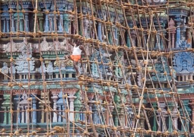 Criss-cross of bamboo scafhold surrounds a temple. A man is visible on the scafhold, working on the temple.